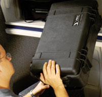 a man putting a Peli storm case into the carry-on overhead luggage compartment on a plane